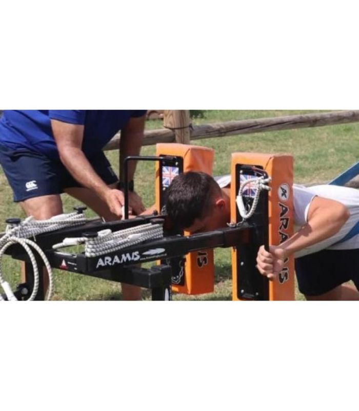Personne pliant une tête mobile JOUG RUGBY SOLO sur un dispositif Aramis, avec un entraîneur debout à côté, en extérieur.