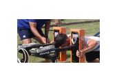 Personne pliant une tête mobile JOUG RUGBY SOLO sur un dispositif Aramis, avec un entraîneur debout à côté, en extérieur.