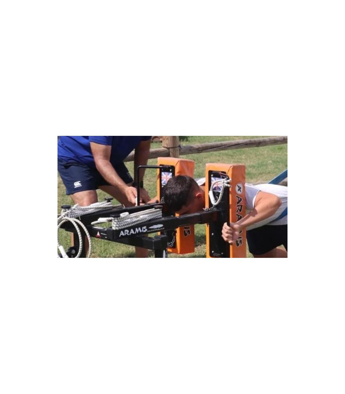 Personne pliant une tête mobile JOUG RUGBY SOLO sur un dispositif Aramis, avec un entraîneur debout à côté, en extérieur.