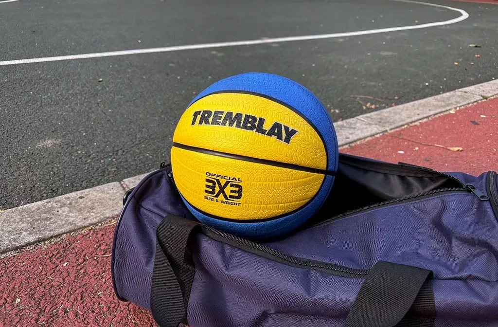 Un ballon de basket jaune et bleu posé sur le bord d’un sac de sport ouvert sur un terrain.