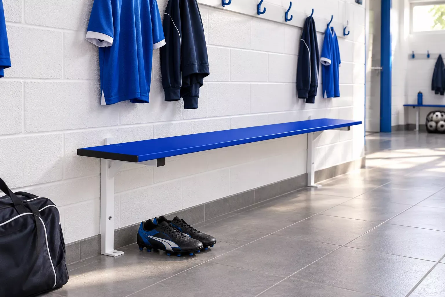 Chaussures de sport et sac sur le sol près d’un long banc bleu dans un vestiaire de sport.