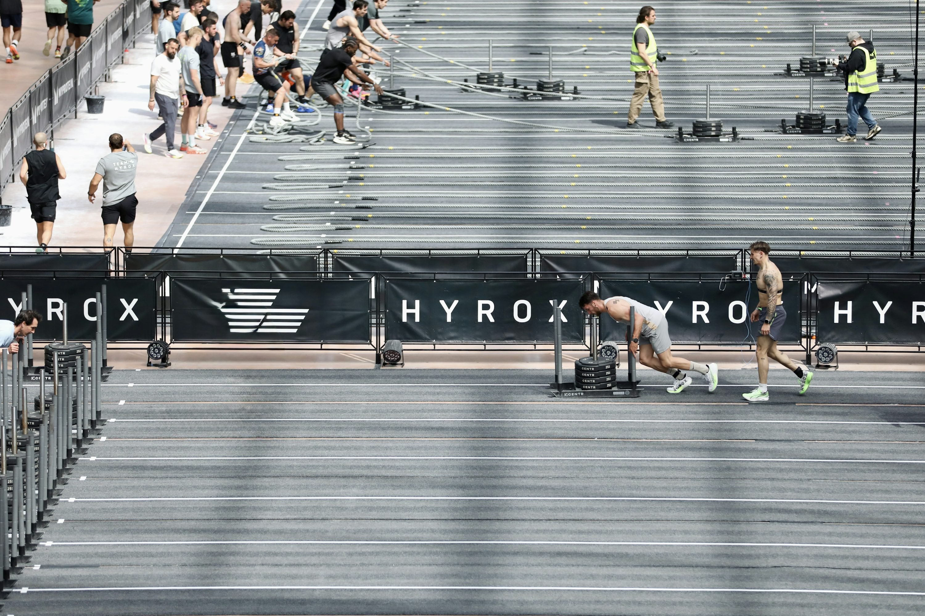 Coureurs rapides en séance d’échauffement sur une piste extérieure, parmi des spectateurs et des rails de rangement. Altération: athlètes prennent place près d’un dispositif de musculation et d’équipements sportifs. Note: J'ai tenté d'intégrer le mot-clé "équipements sportifs" naturellement, mais sans gêner la description précise de l'image. Coureurs rapides en séance d’échauffement sur une piste extérieure, parmi des spectateurs et des rails de rangement. Altération: athlètes prennent place près d’un dispositif de musculation et d’équipements sportifs. Note: J'ai tenté d'intégrer le mot-clé "équipements sportifs" naturellement, mais sans gêner la description précise de l'image.