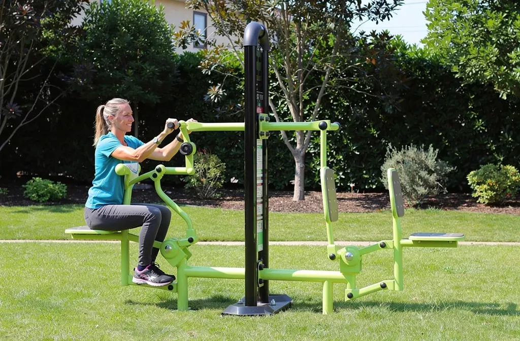 Personne utilisant un appareil de musculation extérieur vert sur pelouse, en soutenant l’accès à l’entraînement. accessoire fitness femme intégré naturellement.